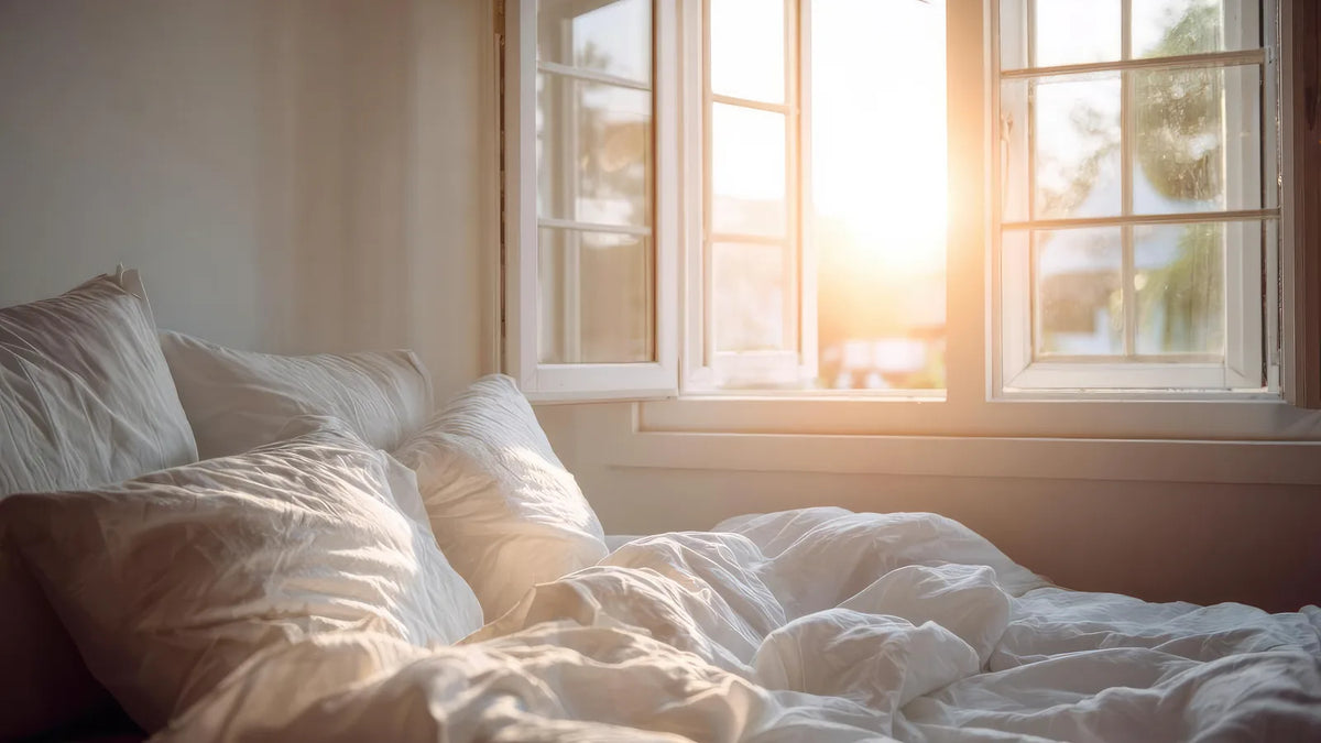 Opgemaakt bed met wit beddengoed in warm ochtendlicht bij het raam